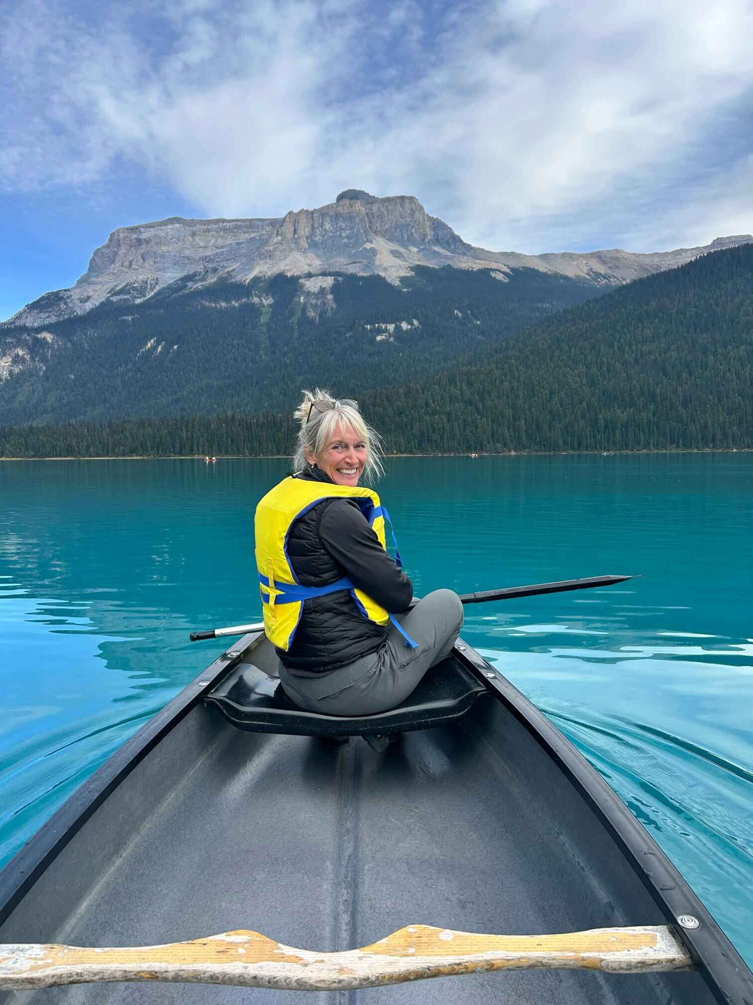 	Paige in a yellow life vest smiling from a canoe on a turquoise lake in Banff